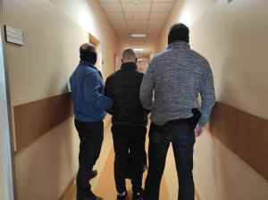 Zdjęcie przestawia trzech mężczyzn, dwaj to policjanci ubrani po cywilnemu, a trzeci stojący między nimi to zatrzymany poszukiwany mężczyzna